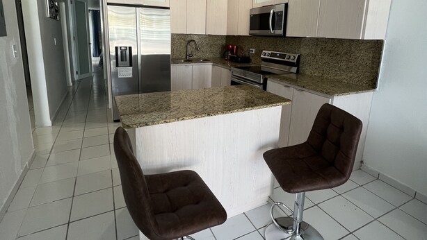Una cocina moderna con una isla central, electrodomésticos de acero inoxidable y dos taburetes de bar.