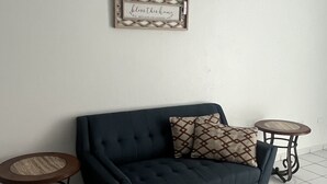 Una sala de estar con un sofá azul oscuro, dos mesas redondas y un cartel decorativo en la pared.