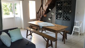 Un espace de vie chaleureux avec une table en bois, un banc et un canapé. Un escalier avec une rampe en bois mène à un niveau supérieur.