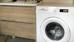 Une salle de bain moderne avec un meuble-lavabo en bois, un lave-linge et un miroir agrémenté d’un pare-feu en carreaux aux motifs géométriques.
