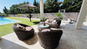 A covered patio area with wicker furniture, a pool, and a wooden fence. - Villa with spa pool petanque court (Narbonne)