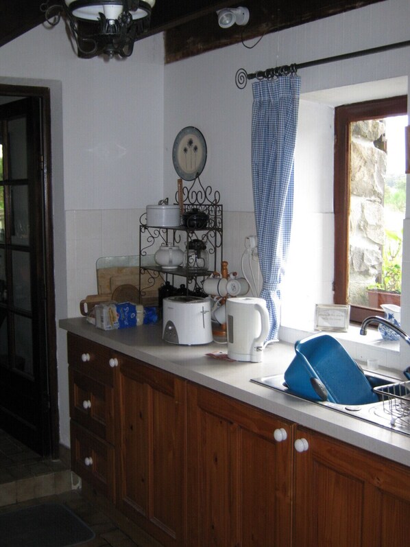 Cocina con armarios de madera, encimera blanca y diversos electrodomésticos.