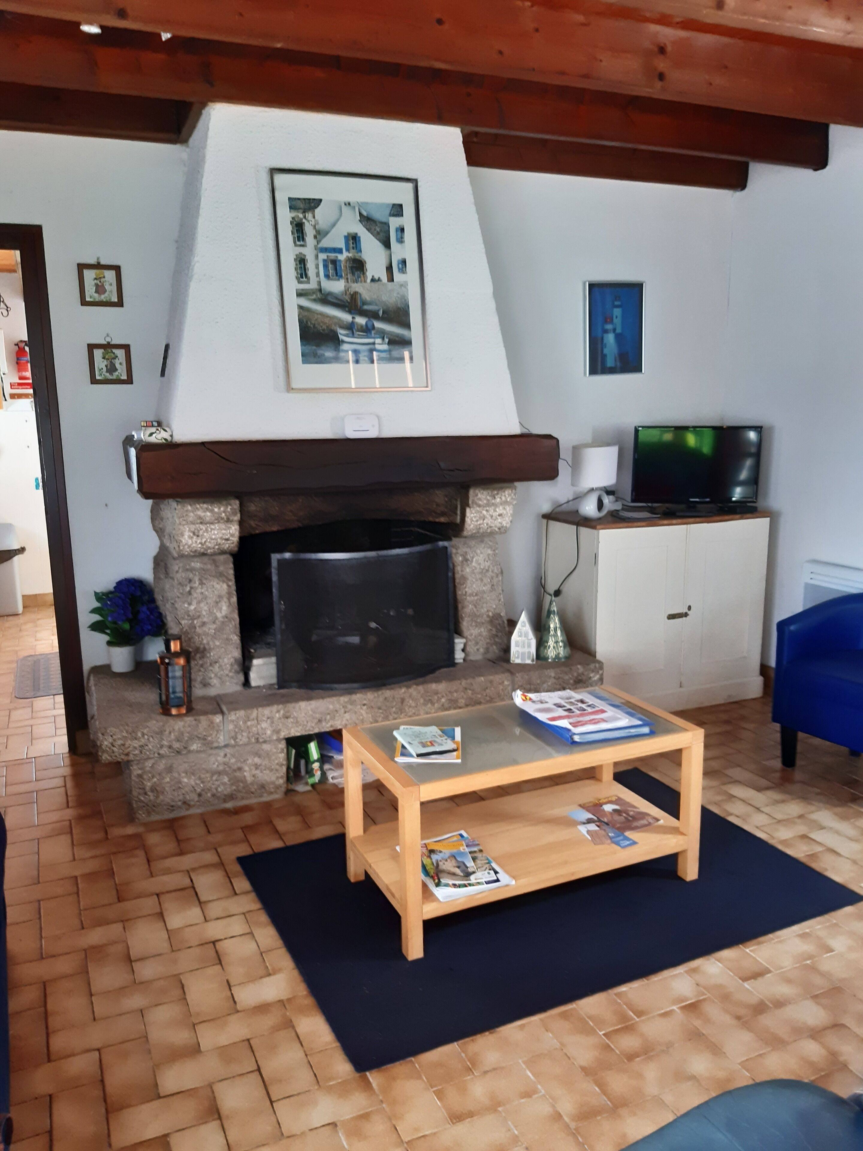 Un salon avec une cheminée en pierre, un téléviseur, un canapé bleu et une table basse avec des magazines.