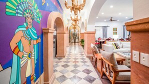Un'hall di hotel con pavimento a scacchi, un affresco, un lampadario e un'area salotto con divani e poltrone.