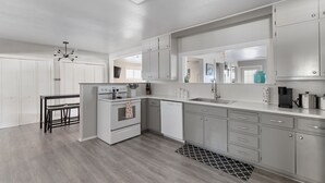 A modern kitchen with grey cabinets, a built-in oven, a dishwasher, and a dining area with a table and chairs.