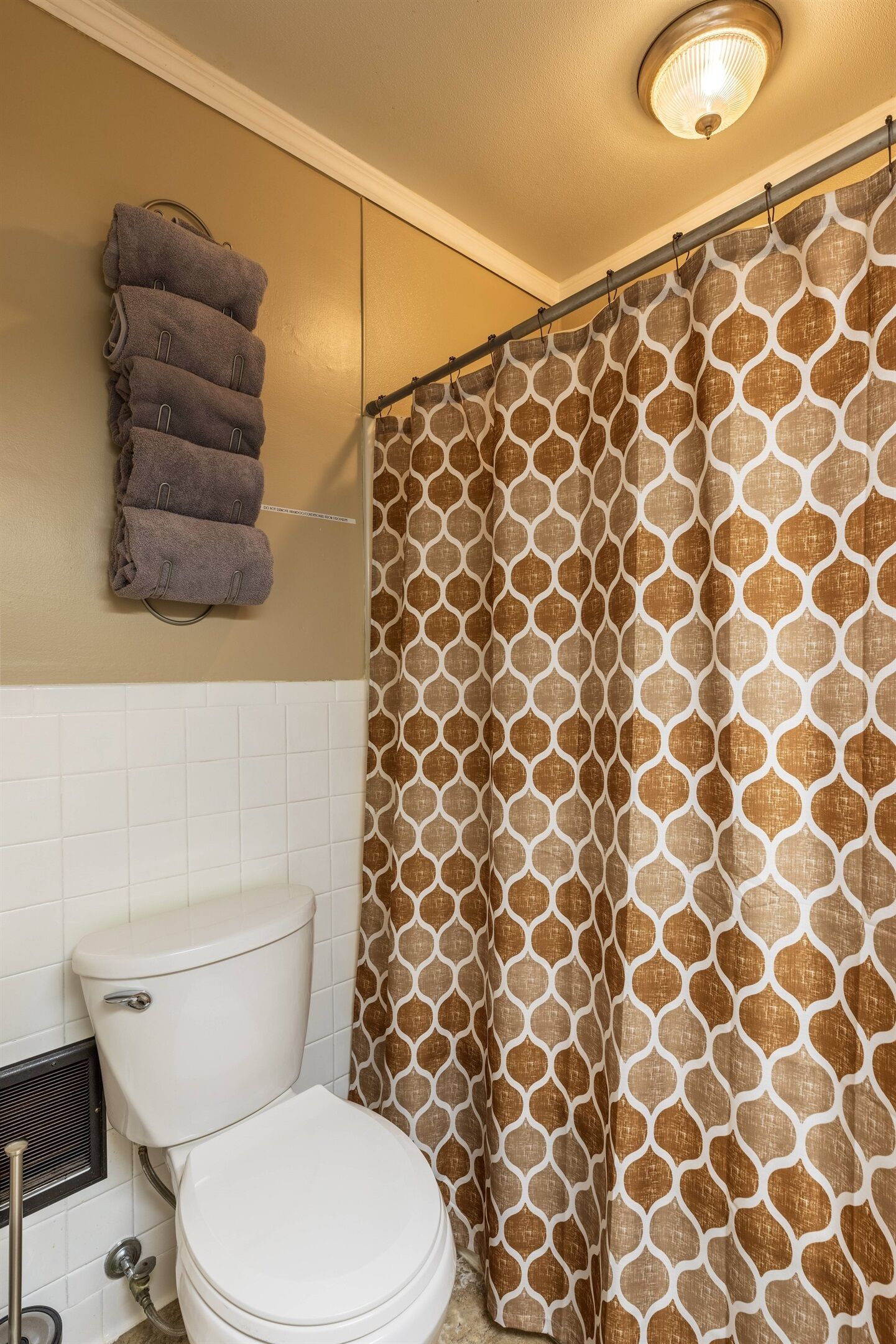A bathroom with a toilet, a towel rack with folded towels, and a shower curtain with a geometric pattern.