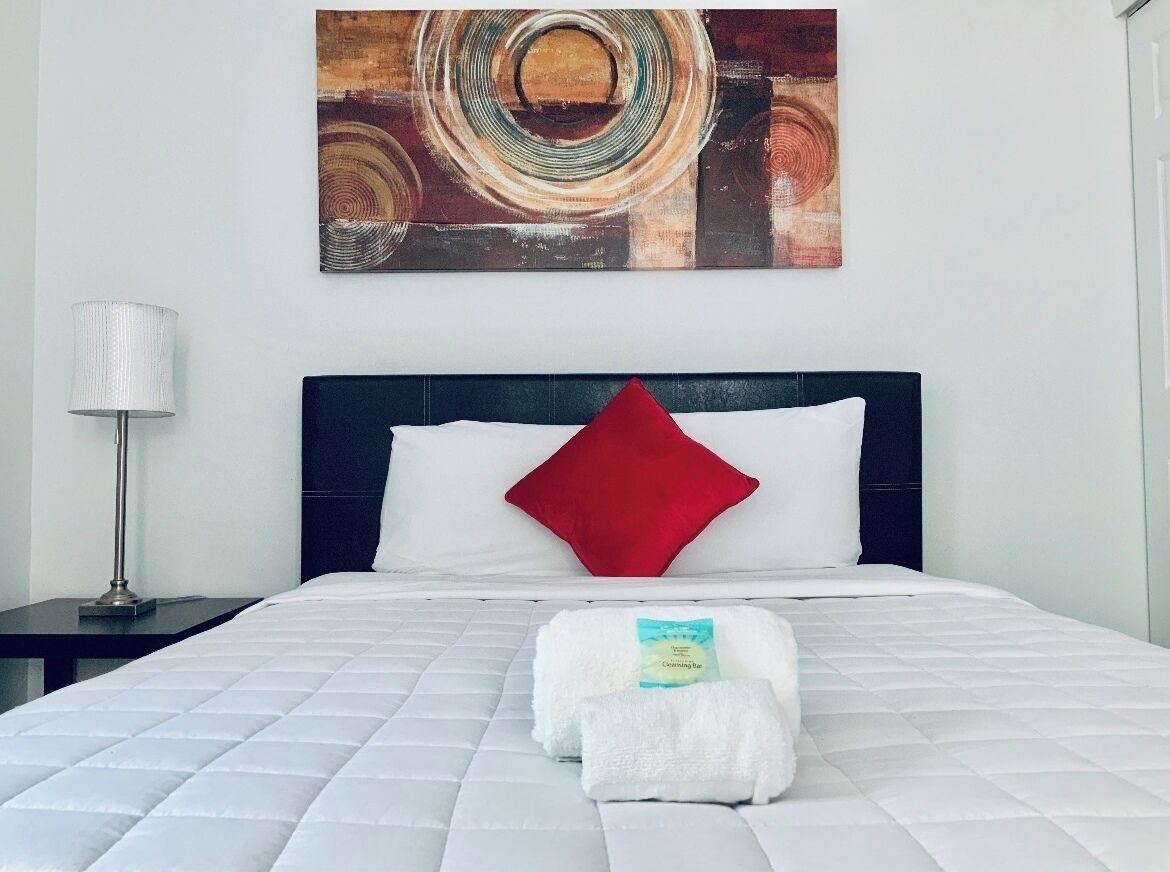 A neatly made bed with a white quilt, a red pillow, and a white towel on the bed.