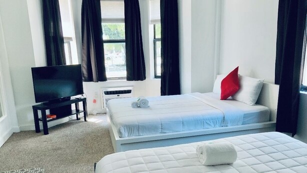 Ein Hotelzimmer mit einem Bett, einem Fernseher, einem kleinen Tisch und einem Fenster mit Vorhängen.