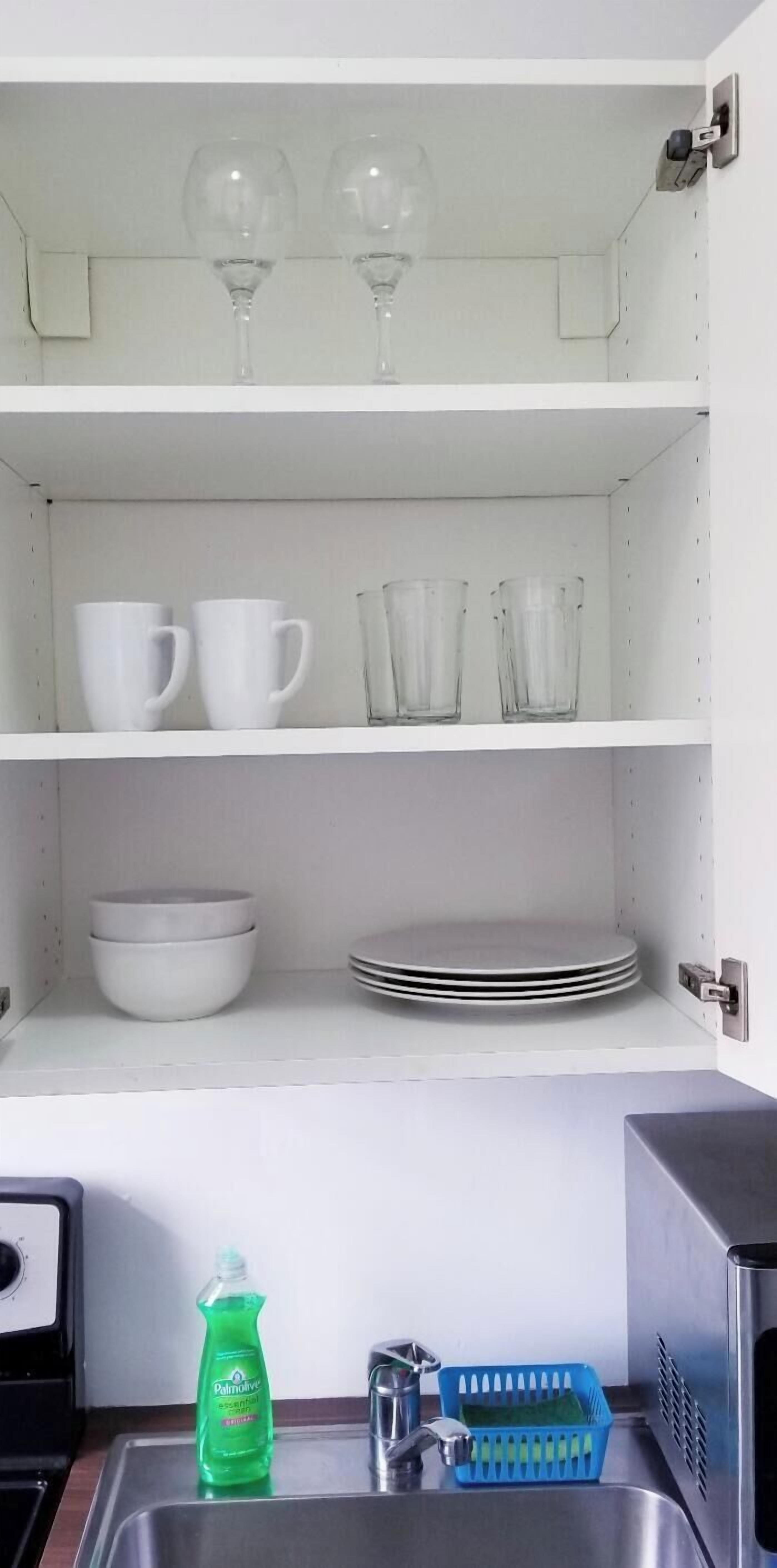 Une cuisine avec des étagères blanches où sont rangées des tasses, des verres, des bols et des assiettes.