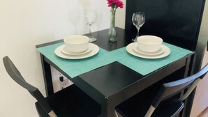 Et lille spisebord med to hvide skåle og to vinglas, en vase med lyserøde blomster, samt en turkis spisebrik.