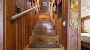 A wooden staircase with a handrail, leading to a bedroom with a bed and a window.