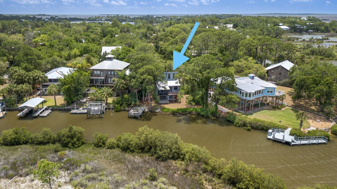 A large house with a dock and boats, surrounded by dense trees and a body of water.
