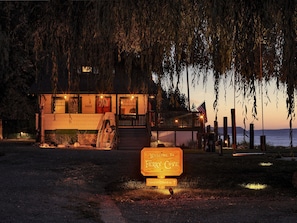 A cabin with a porch, a sign reading "Welcome to Ferry Cove", and a view of the water.