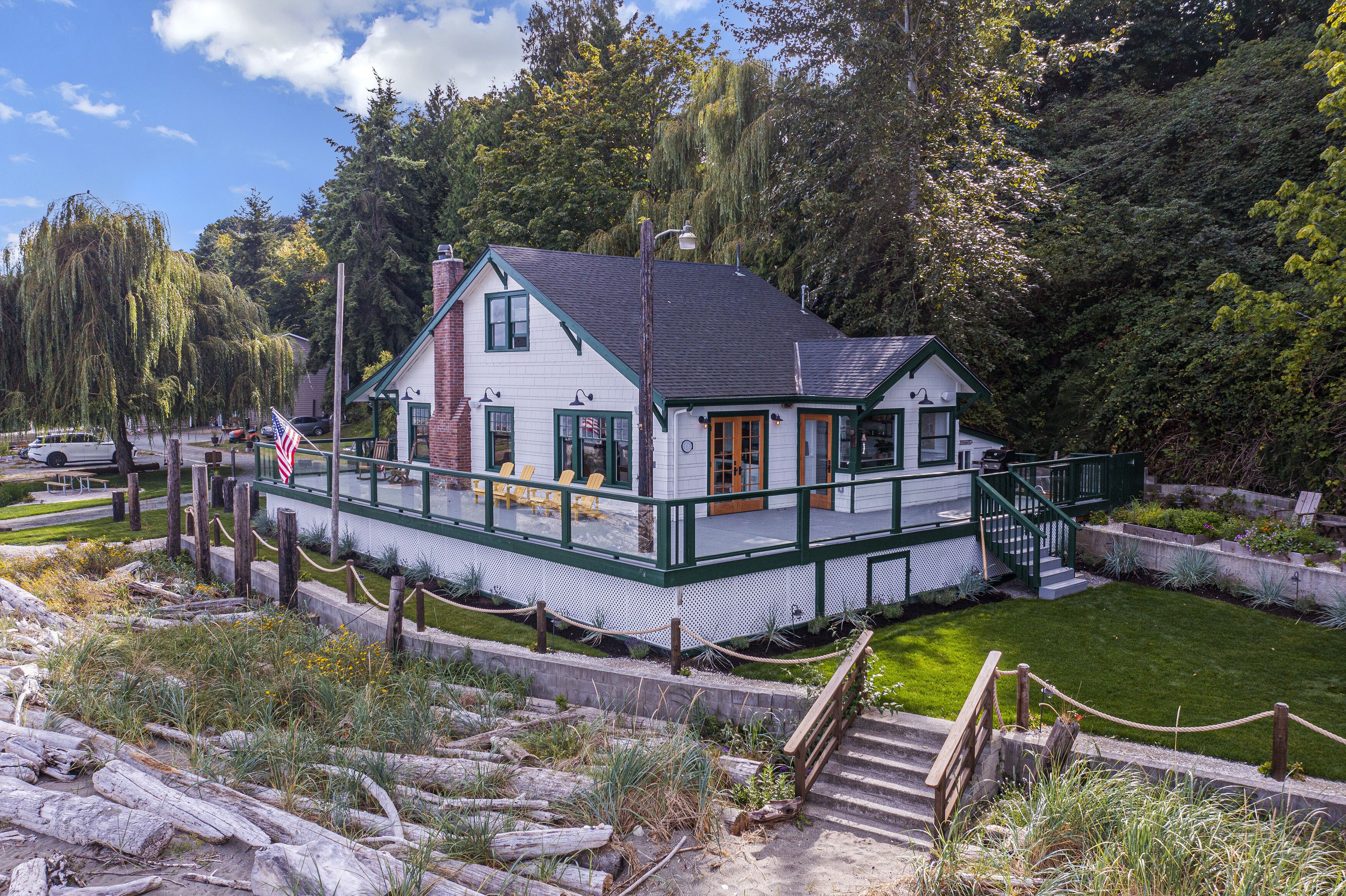 A white house with a green porch, surrounded by trees and a grassy area.