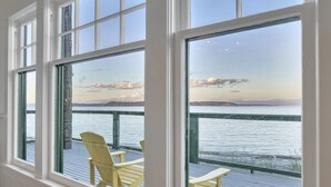 A room with large windows overlooking a deck with chairs. - Ferry Cove - Private low bank beachfront property. (Clinton)