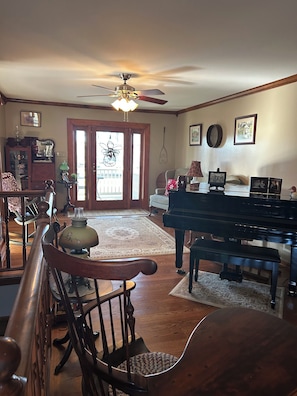 A living room with a piano, wooden chairs, a dining table, a ceiling fan, and a view through a glass door. - Old Homestead...Rest, relax and renew at this quaint getaway. (Shippensburg)