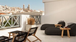 Terraza en la azotea con un sofá negro, sillas de madera y una mesita con una copa y uvas.