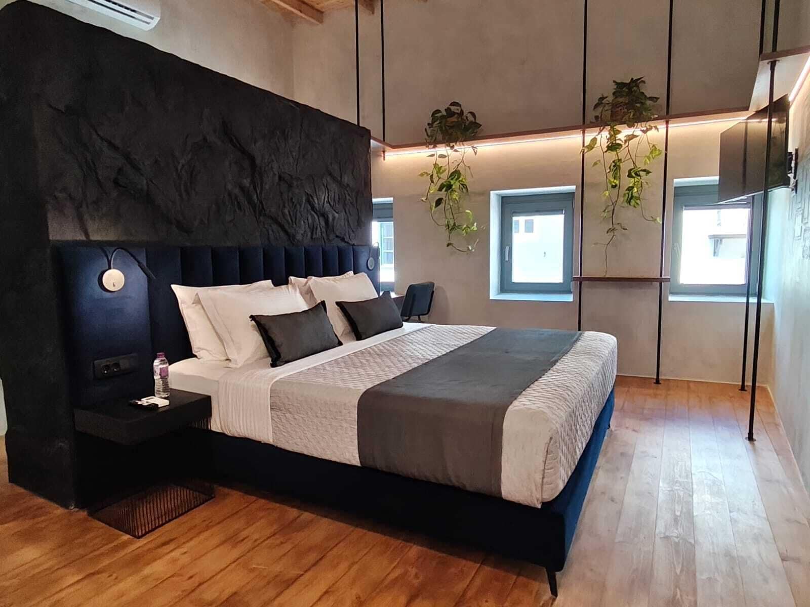 Ein modernes Schlafzimmer mit einem großen Bett, Nachttischen, einer Wandheizung und hängenden Pflanzen.