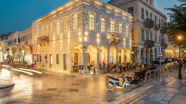Un edificio de piedra con ventanas arqueadas y un balcón, rodeado de motocicletas estacionadas y una zona peatonal.