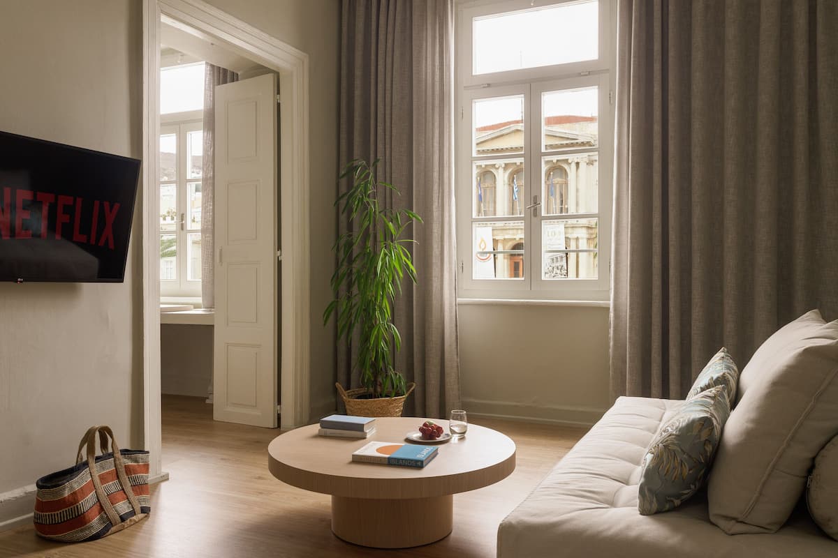 A living room with a round coffee table, a sofa, a television, a plant, and a view of a building through a window.