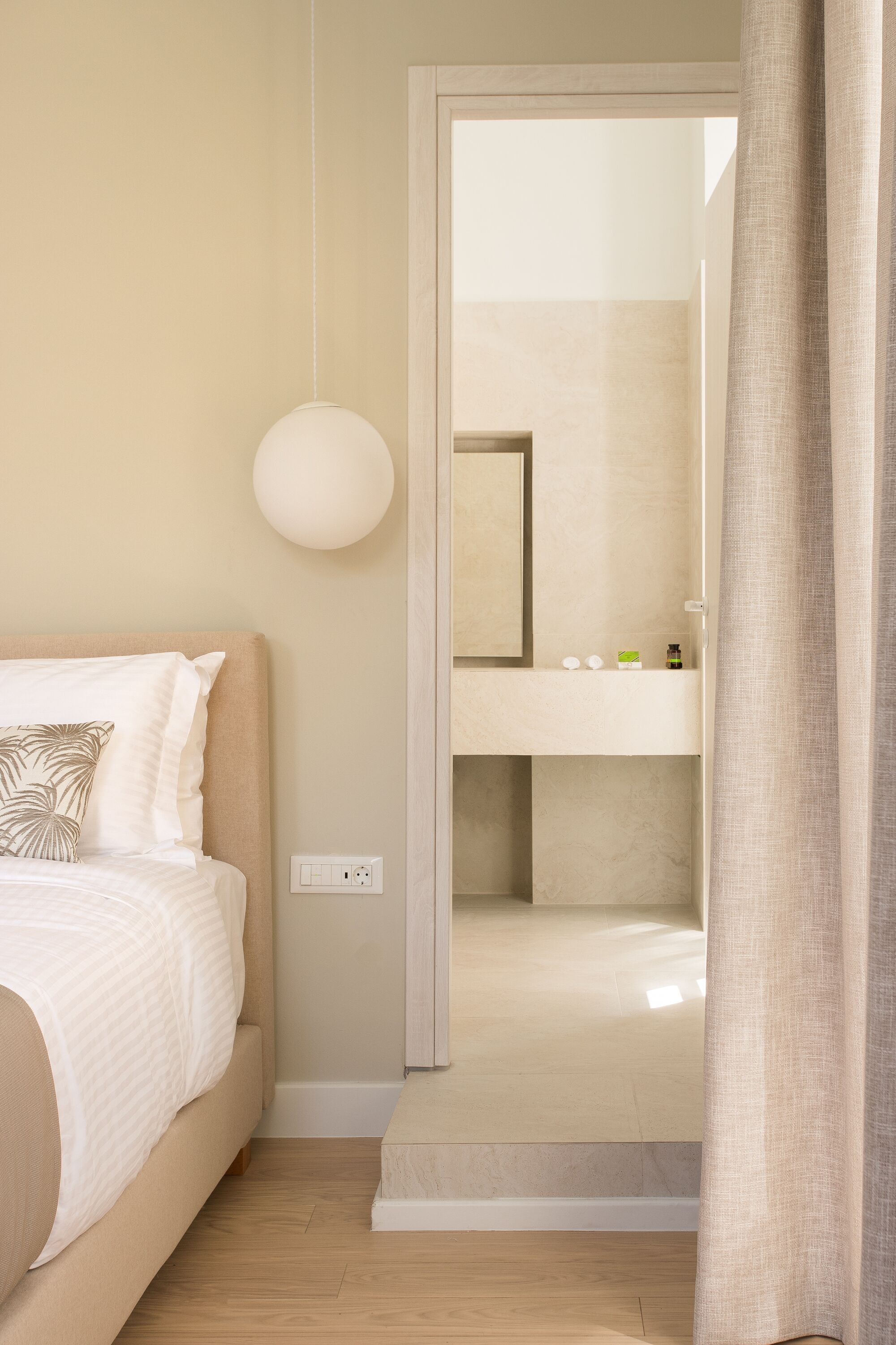 Une chambre d’hôtel avec un lit, une table de chevet, un miroir et une salle de bain visible à travers une porte ouverte.