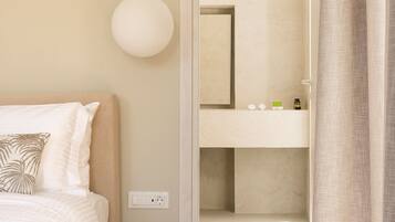 Une chambre d’hôtel avec un lit, une table de chevet, un miroir et une salle de bain visible à travers une porte ouverte.