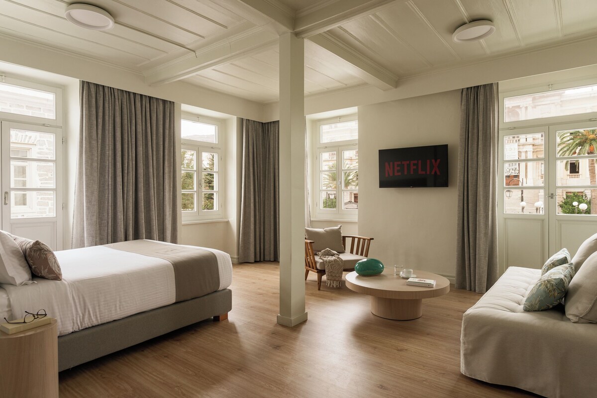 A modern hotel room with a large bed, a sofa, a round coffee table, and a TV mounted on the wall.