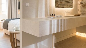 Un baño moderno con pared de piedra, un espejo grande, un lavamanos blanco y una mesita de noche con lámpara.