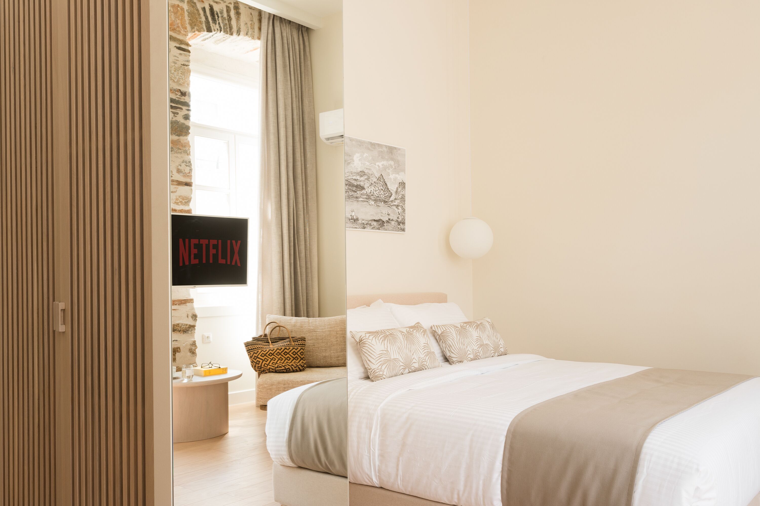 Ein modernes Schlafzimmer mit einem Bett, einem Nachttisch und einem an der Wand montierten Fernseher, der 'NETFLIX' zeigt.