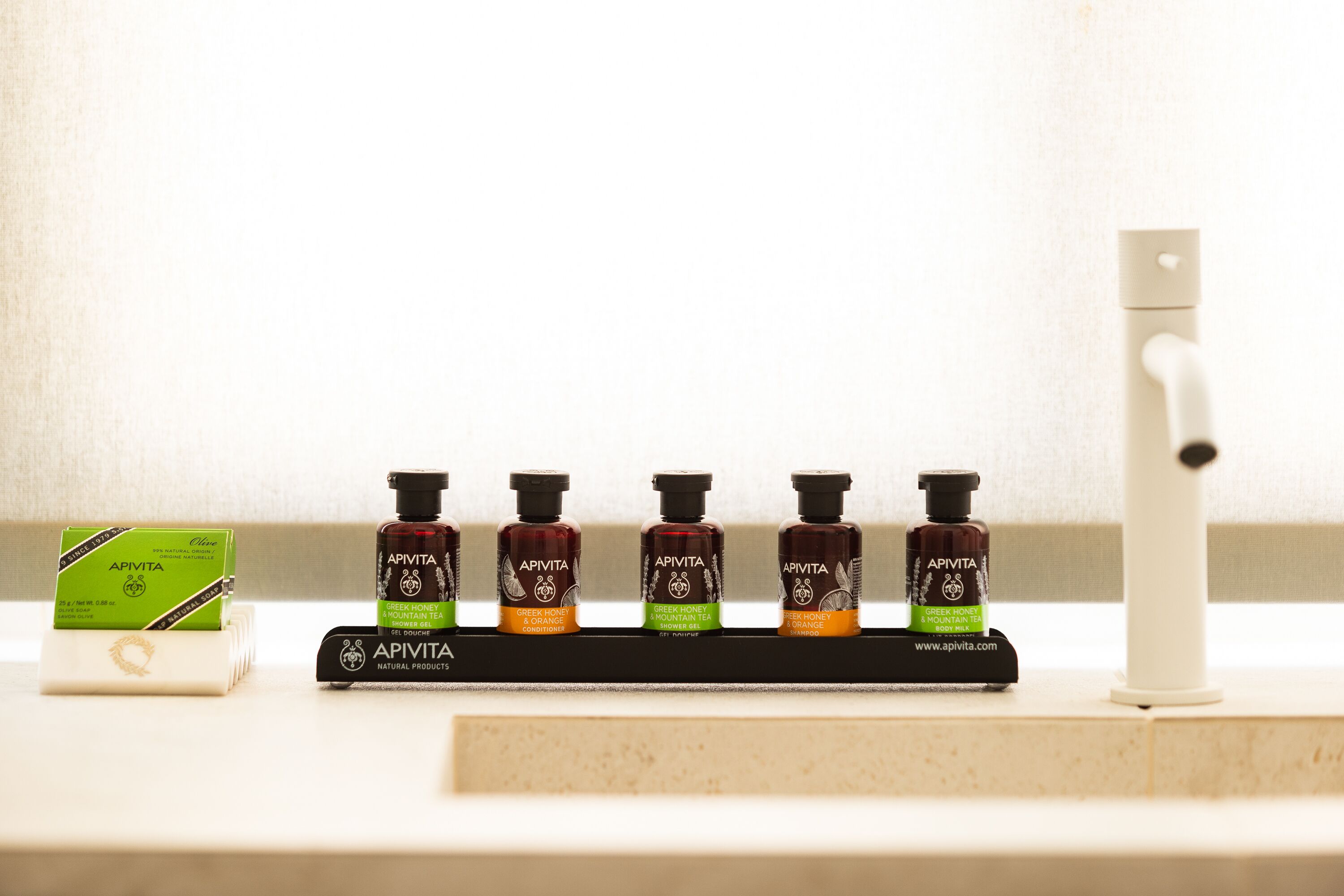 A shelf with four bottles of Apivita products and a green box on a countertop.