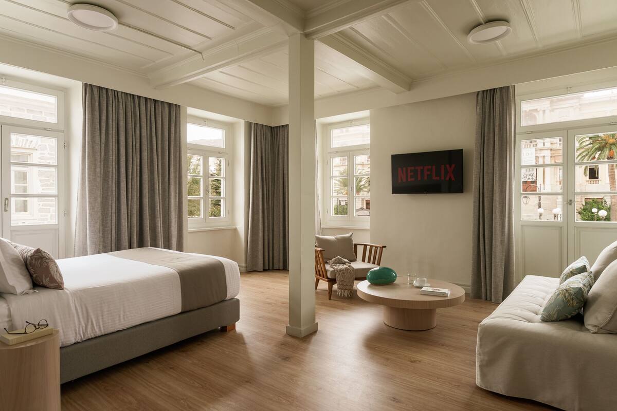 A modern hotel room with a large bed, a sofa, a round coffee table, and a TV mounted on the wall.