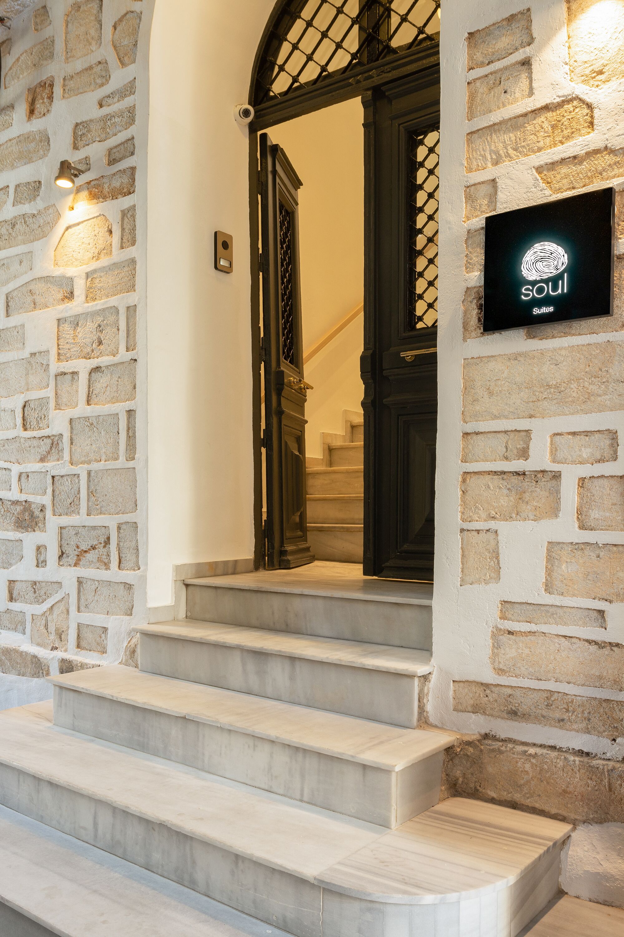 A stone wall with a sign reading "soul Suites" above a set of marble stairs leading to a dark wooden door.