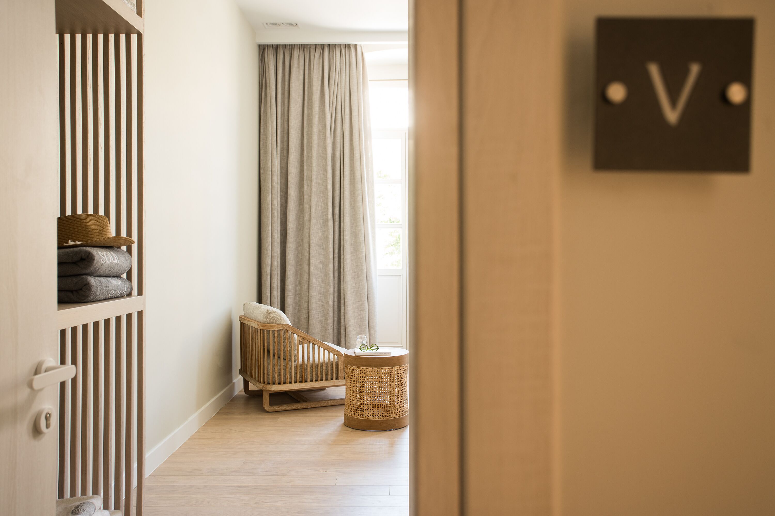 Une chambre avec un berceau, une table d’appoint en osier et un signe en forme de « V » sur le mur.