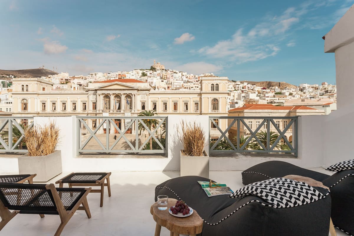 A rooftop terrace with outdoor seating, a view of a historic cityscape, and a clear sky.