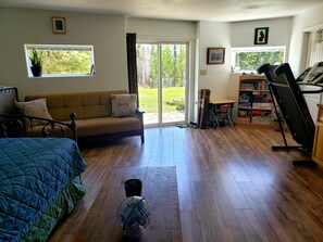 Relax in this serene room featuring a large bed, a sofa, and a treadmill, with a sliding door leading to a backyard.