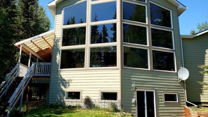 A two-story house with a large glass window section, a covered porch, and a satellite dish. - Windows With a View (Soldotna)
