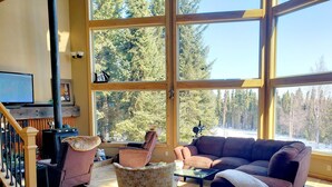 A spacious living room with a large window, a fireplace, a sofa, and a coffee table. - Windows With a View (Soldotna)