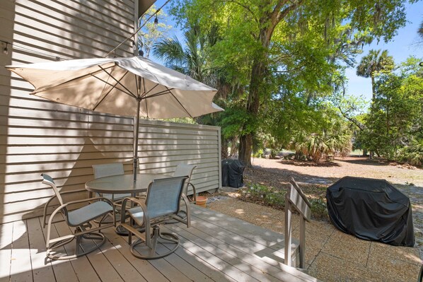 A patio with a table and chairs, a covered grill, and a wooden deck.
