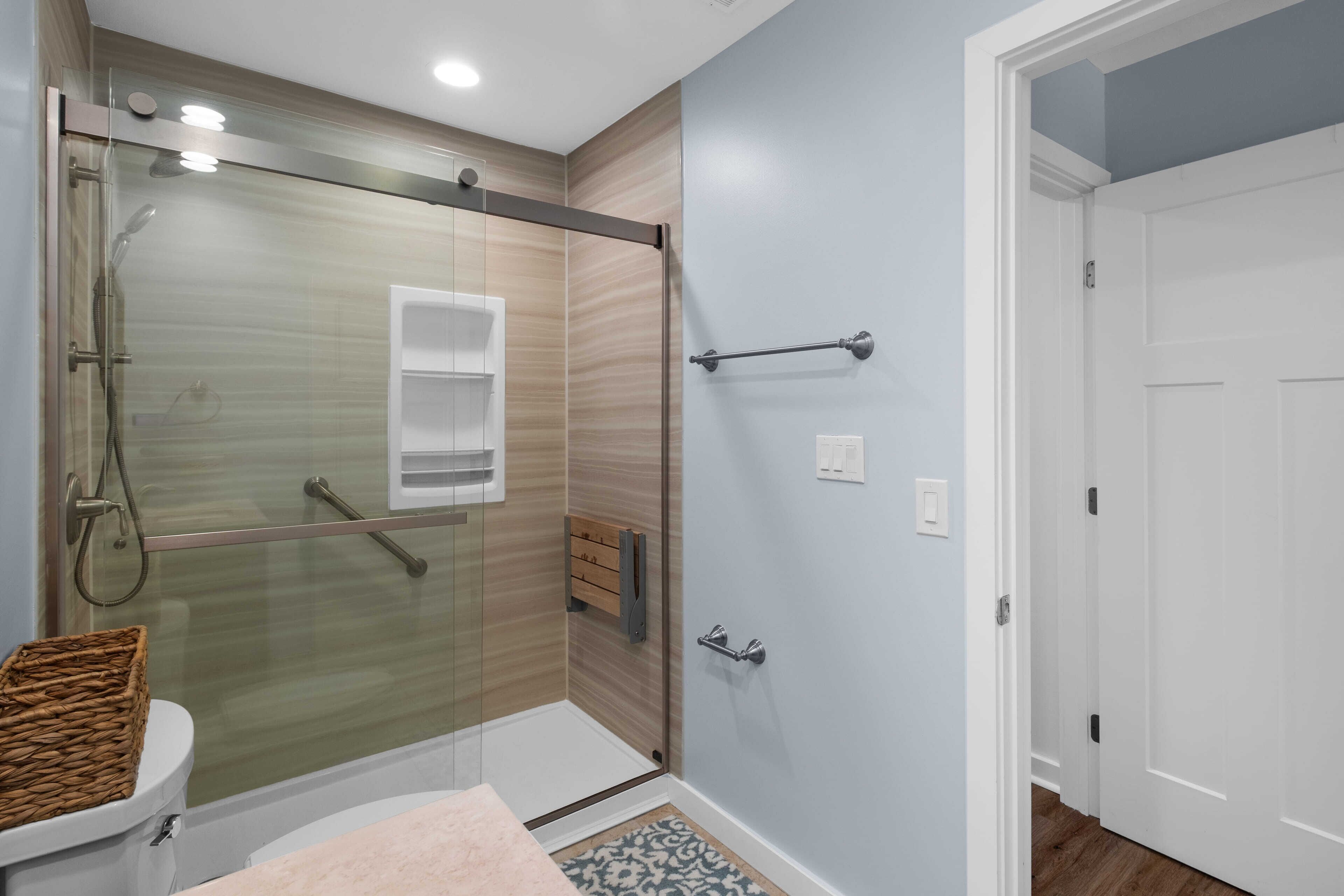 A bathroom with a glass shower enclosure, a toilet, a basket, and a towel rack.
