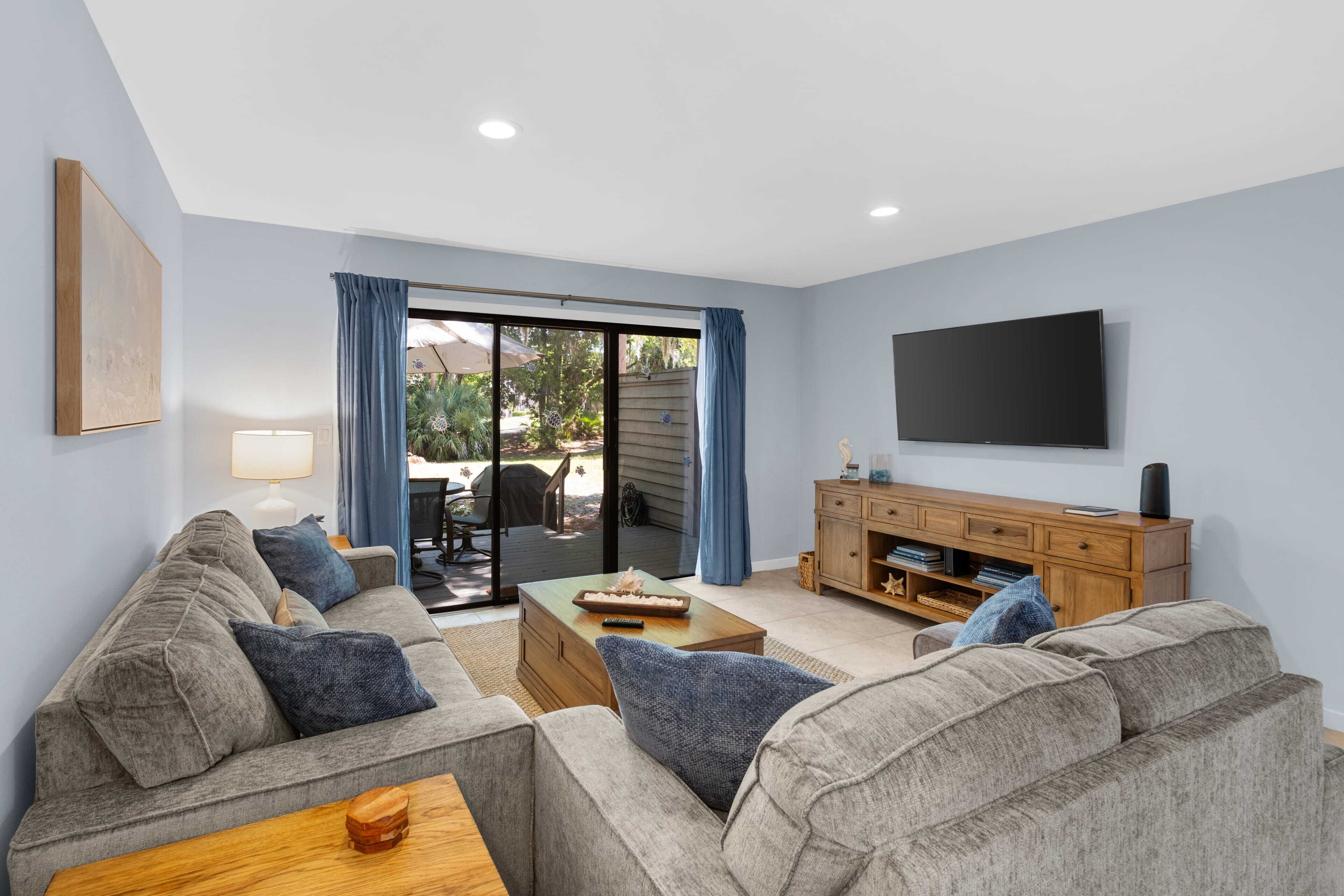 A living room with a sofa, coffee table, TV, and a sliding glass door leading to an outdoor area.