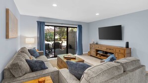 Ein Wohnzimmer mit Sofa, Couchtisch, Fernseher und einer Schiebetür zu einem Außenbereich.