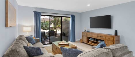 A living room with a sofa, coffee table, TV, and a sliding glass door leading to an outdoor area.