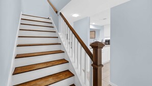 Eine Treppe mit Holzboden und Holzwand handläufen, die zu einem Küchenbereich mit weißen Schränken und einem gefliesten Boden führt.
