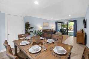 Un comedor con una mesa de madera preparada para cuatro personas, un sofá y un televisor montado en la pared.