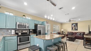 Una cocina moderna con armarios color turquesa, electrodomésticos de acero inoxidable y una isla central con taburetes.