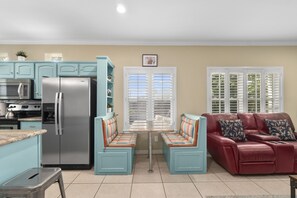 A kitchen with a refrigerator, stove, and microwave. There is a dining table with benches and a red leather sofa with cushions.