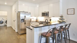 Une cuisine moderne avec des meubles blancs, des appareils en acier inoxydable et un îlot central doté de tabourets de bar.