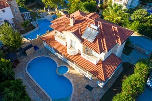 A house with a swimming pool, a covered patio, and a red-tiled roof.