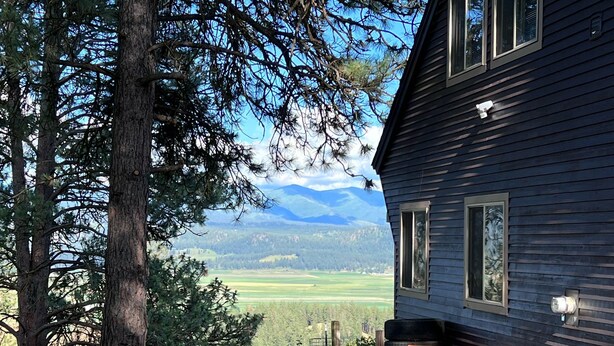 A house with a gravel driveway, a wooden deck, and a view of mountains in the background.
