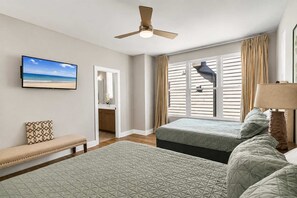 Ein Schlafzimmer mit zwei Betten, einem Deckenventilator, einem Fernseher und einem Fenster mit Jalousien.